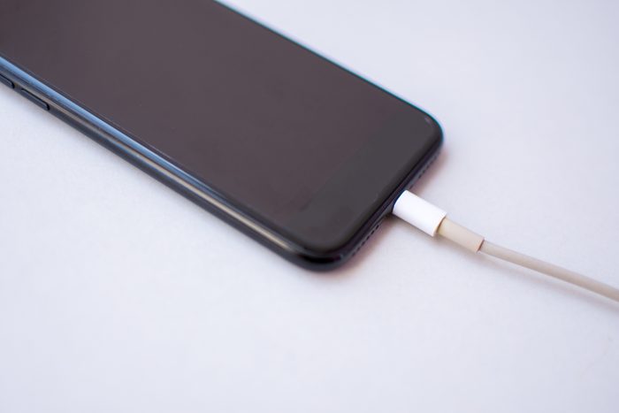 High Angle View Of Smart Phone Charging Against White Background