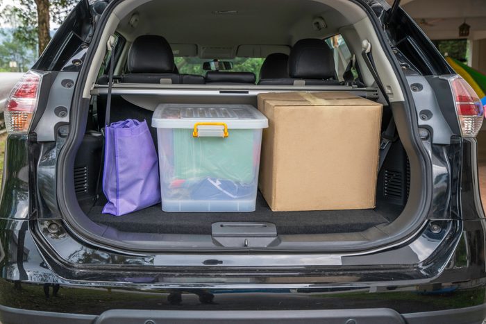 organized car trunk with a purple reusable grocery bag, plastic bin and cardboard box