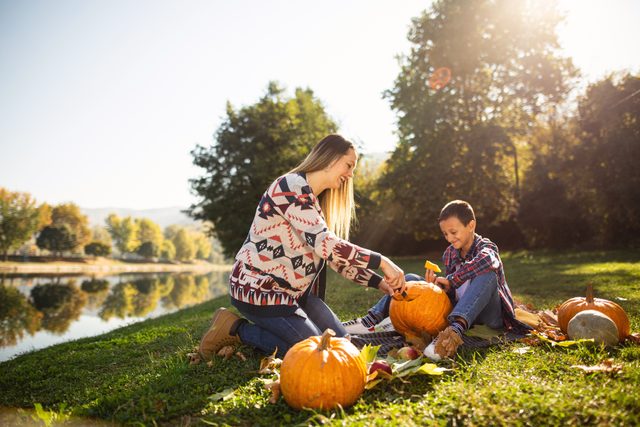mother and son carving jack-o-lanterns in a field by a lake