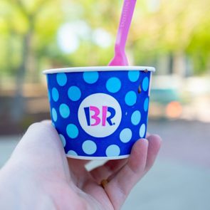 Close-up of hand holding a container of Baskin Robbins brand ice cream with logo in outdoor setting