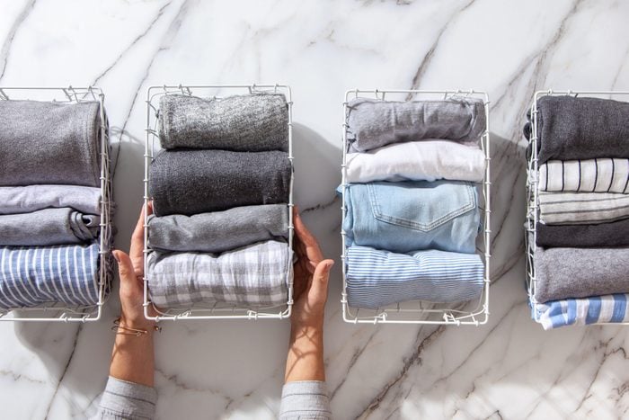 Neatly folded clothes and pyjamas in the metal mesh organizer basket on white marble table