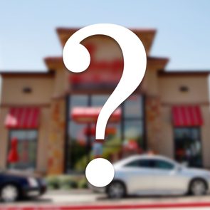 a blurred image of a restaurant facade with cars in the drive thru with a question mark overlay