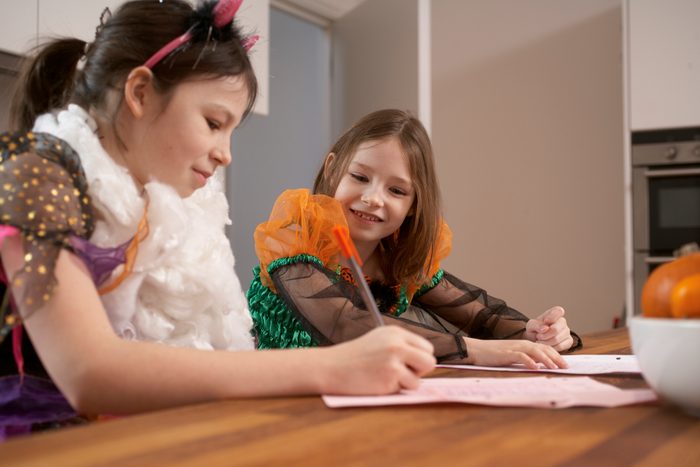young girls in halloween costumes writing down movie quotes for party game