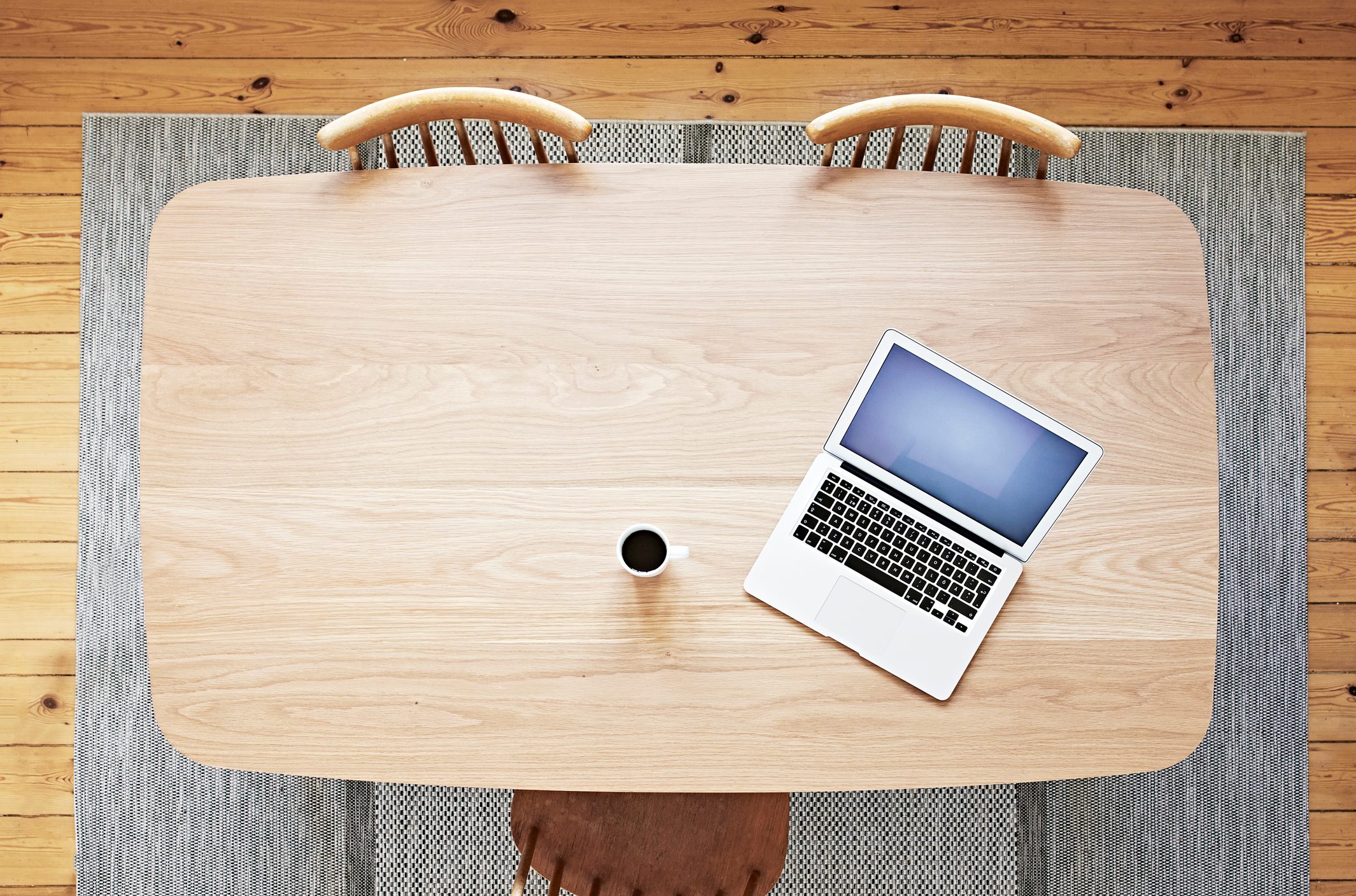 Laptop and coffee on wooden table with wooden chairs surrounding