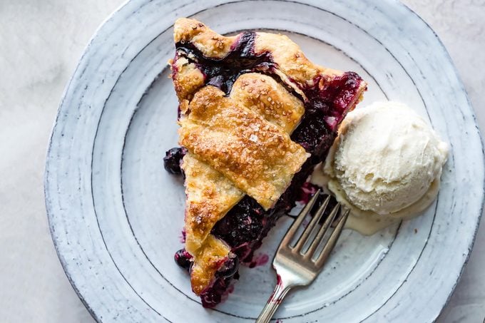 slice of huckleberry pie with vanilla ice cream and a fork on a plate