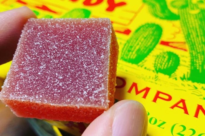 close up of fingers holding a square Cactus Candy gummy with the box in the background