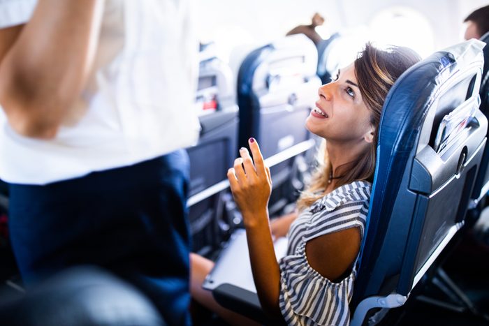 Happy woman talking to flight attendant in an airplane.