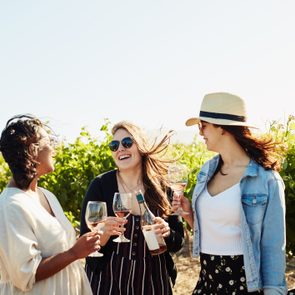 three girlfriends laughing while drinking wine at a winery vineyard
