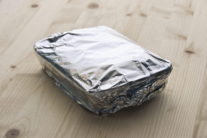 tray of leftover food covered with aluminum foil on a wood counter