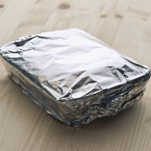 tray of leftover food covered with aluminum foil on a wood counter