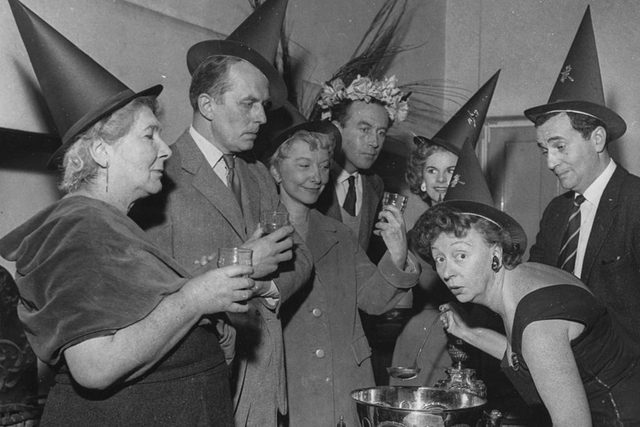 Actress Thora Hird (right, bending down) serving a witches brew punch at a Halloween party with fellow actors
