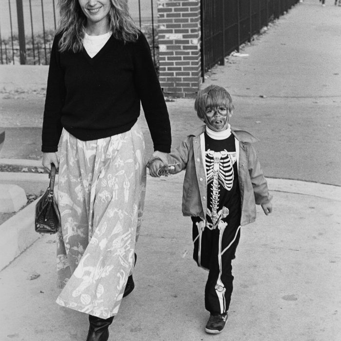 Child dressed as a skeleton for Halloween, holding a woman's hand and walking down Armitage Avenue near Halsted Street, Chicago, Illinois, October 1987.