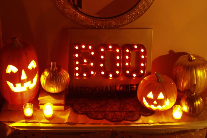 Halloween Marquee Lights spell out "BOO" and sits on a table surrounded by jack-o-lanterns, pumpkins, and candles
