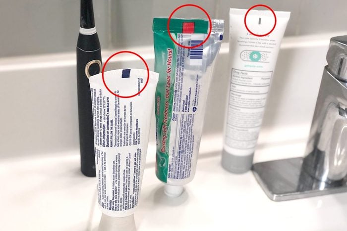 three tubes of toothpaste on a bathroom counter next to the sink; the colored rectangles on the back of each are highlighted with red circle overlays
