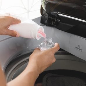 man pouring laundry detergent into HE washing machine