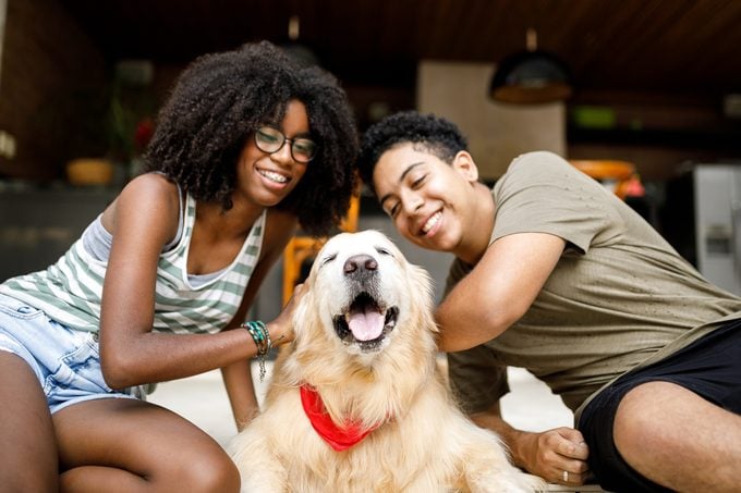 Two people smiling with their golden retriever dog