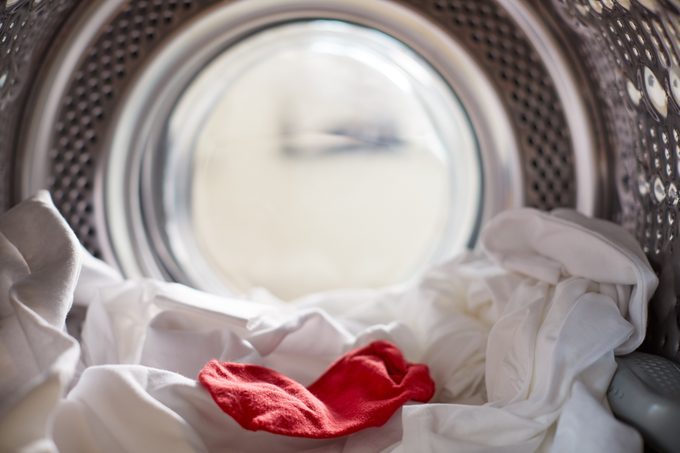 Vista interior de lavadora con calcetín rojo mezclado con lino blanco