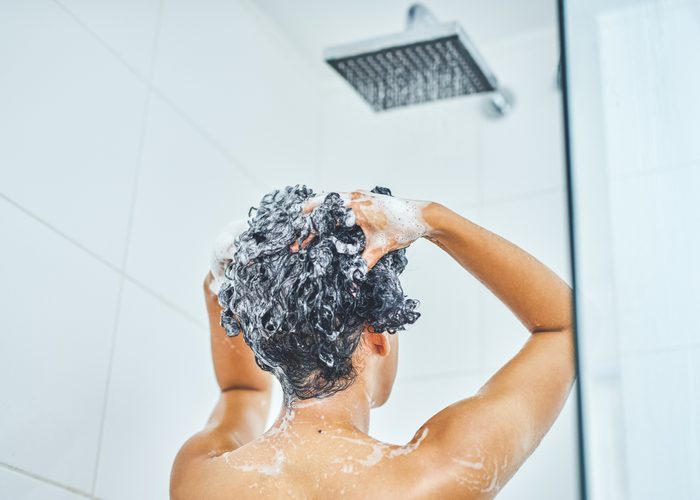 person from behind washing their hair with shampoo in the shower at home