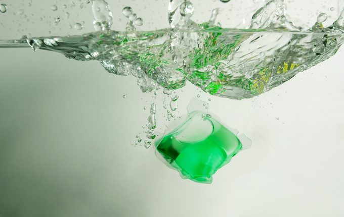 Green laundry detergent pod in water with splash.