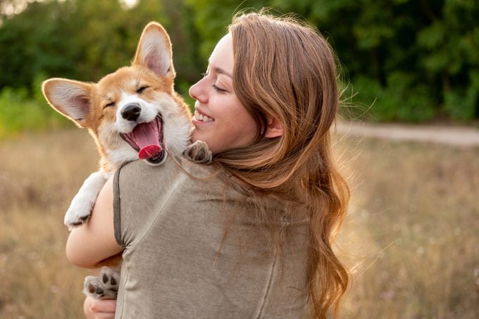 young woman with holding her corgi in a field