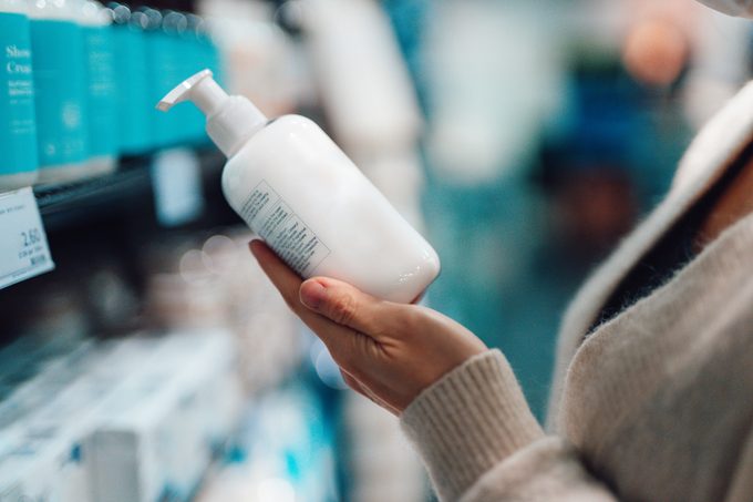 Close-up Of Female Hand Holding a shampoo Bottle In a Supermarket