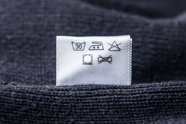 close up of laundry symbols on a care tag of a dark gray wool sweater