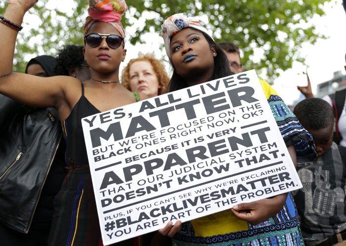 Two women hold a placard with the slogan "Yes, all lives matter" as people gather in protest