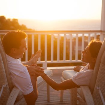 Couple on a romantic getaway vacation smiling with each other while watching the sunset at a resort