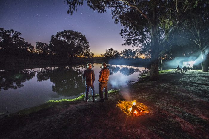 Two men stand by a campfire and watch the stars