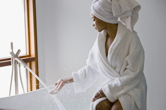 young woman wearing a bath robe filling the bath tub up with water for a spa day