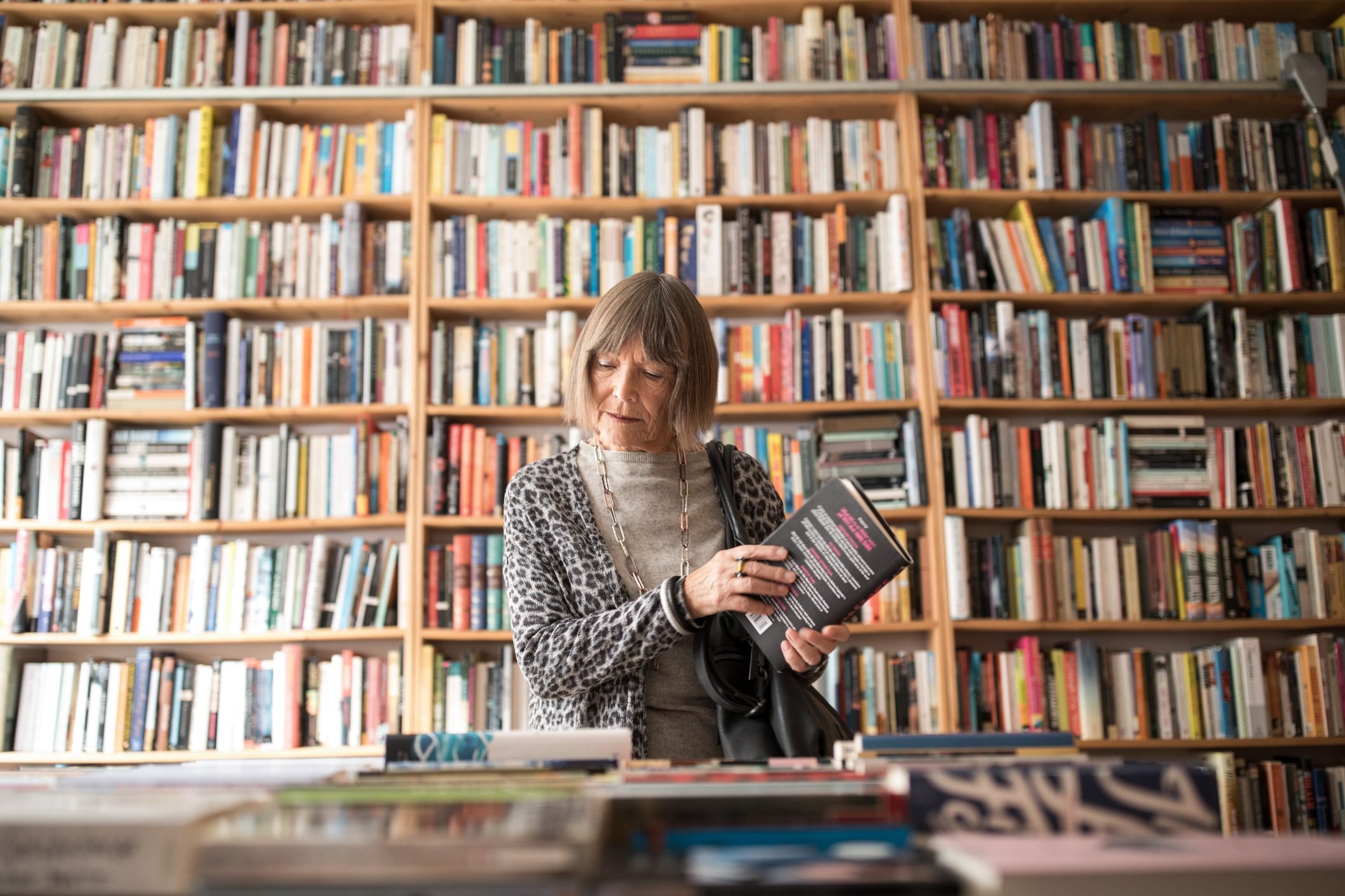 Senior woman with book standing against bookshelf in a book store