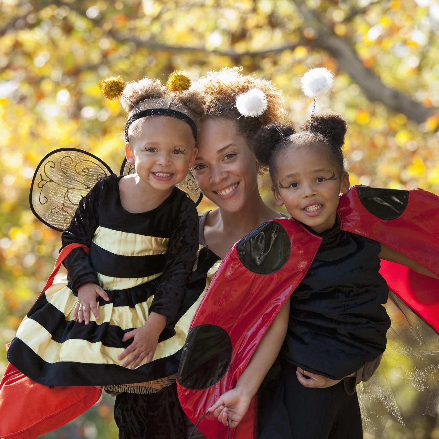 mother smiling with her two daughters dressed up as a bumble bee and a lady bug for halloween