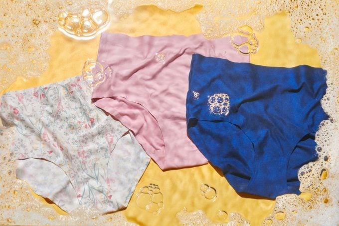 Three pairs of underwear on yellow background with soap bubbles and water effect