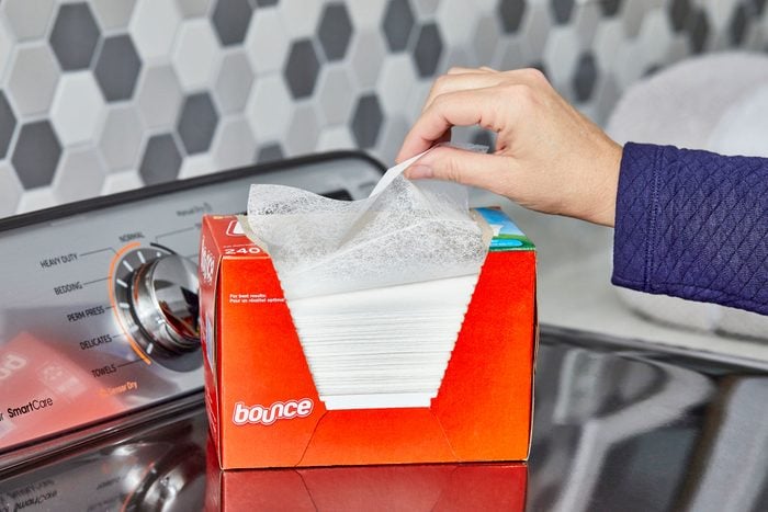 hand pulling a dryer sheet out of the box which is sitting on a washing machine in a laundry room