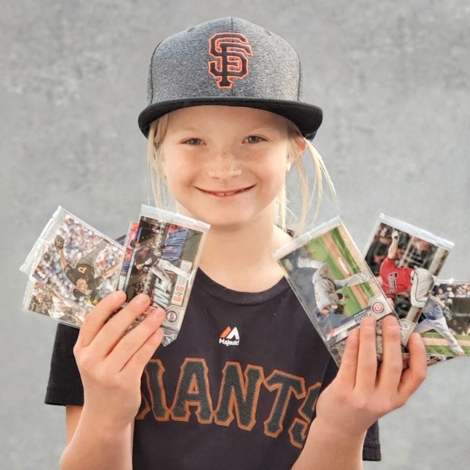 little girl wearing San Francisco baseball hat and shirt showing off a collection of baseball cards.