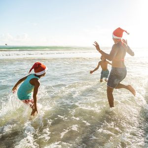 family splashing in the ocean on a sunny day wearing santa hats with their bathing suits