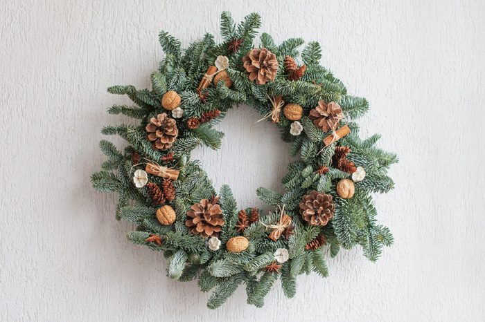 Christmas wreath made of natural fir branches hanging on a white wall. Wreath with natural ornaments: bumps, walnuts, cinnamon, cones. New year and winter holidays. Christmas decor