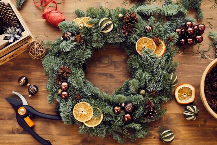 High angle view of beautiful holiday wreath decorated orange slices, fir tree cones and small balls placed on wooden table among decorations and tools