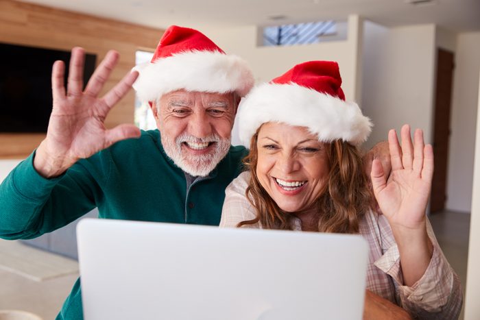 Senior Hispanic Couple Wearing Santa Hats With Laptop Having Video Chat With Family At Christmas