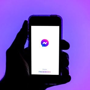 silhouette of a person's hand holding a smarphone with facebook messenger app on screen; blue and purple gradient background