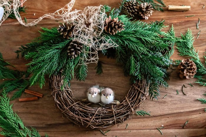 Top view of handmade Christmas wreath made of twigs, pine cones, cinnamon sticks, yew and thuja branches, natural string and wool toys. DIY home decor.