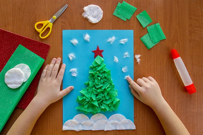 little child making winter decoration "Christmas Tree" from paper, crumpled paper or napkins, and cotton disc