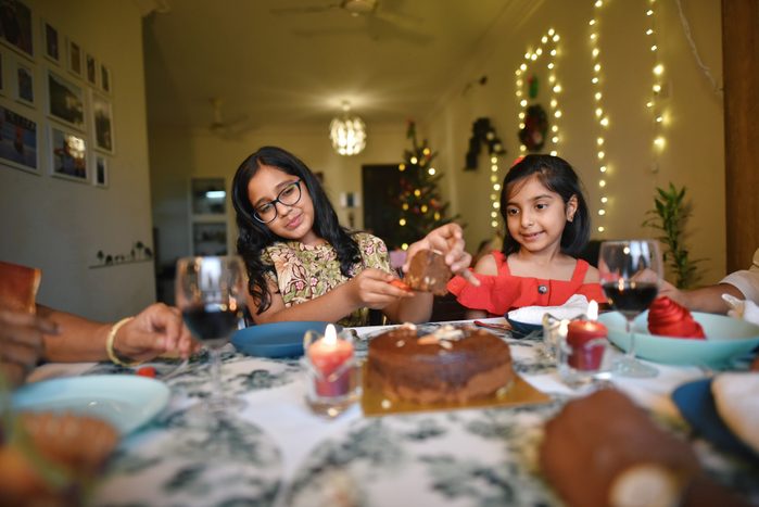 Girls enjoying plum cake with dinner together with family on Christmas Eve in a house decorated with Christmas tree and string lights