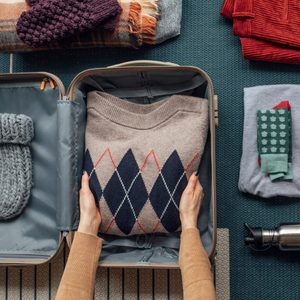 hands placing a folded sweater in a suitcase with other folded clothes nearby