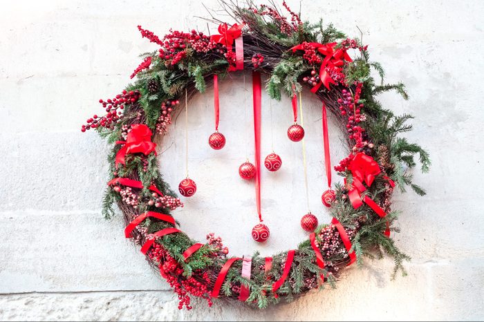 Christmas tradition wreath and balls hanging at wall house background. Traditional rustic xmas wreath of tree branches and red berries, front view