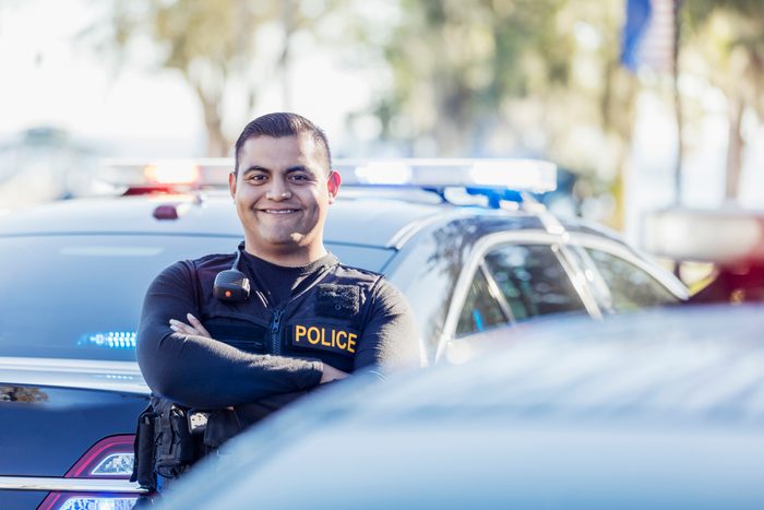 Hispanic police officer standing next to patrol car