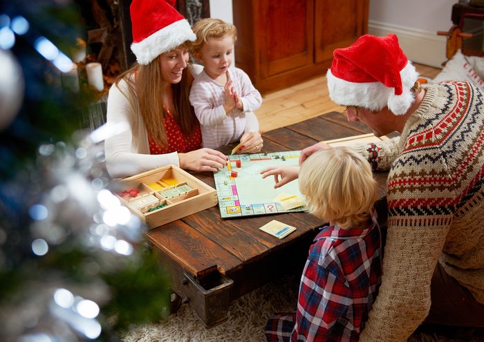 Family with board game, parents in Christmas hats.