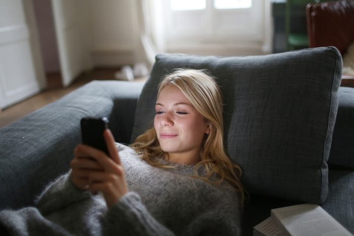 young woman looking at phone while lying on the couch at home
