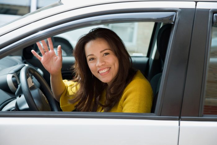 Hispanic woman driving and waving