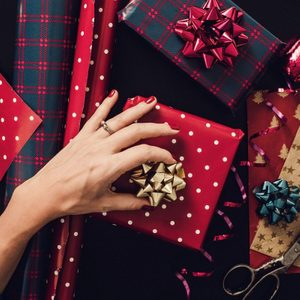 hand adding a bow to a wrapped gift with another gift and rolls of wrapping paper nearby